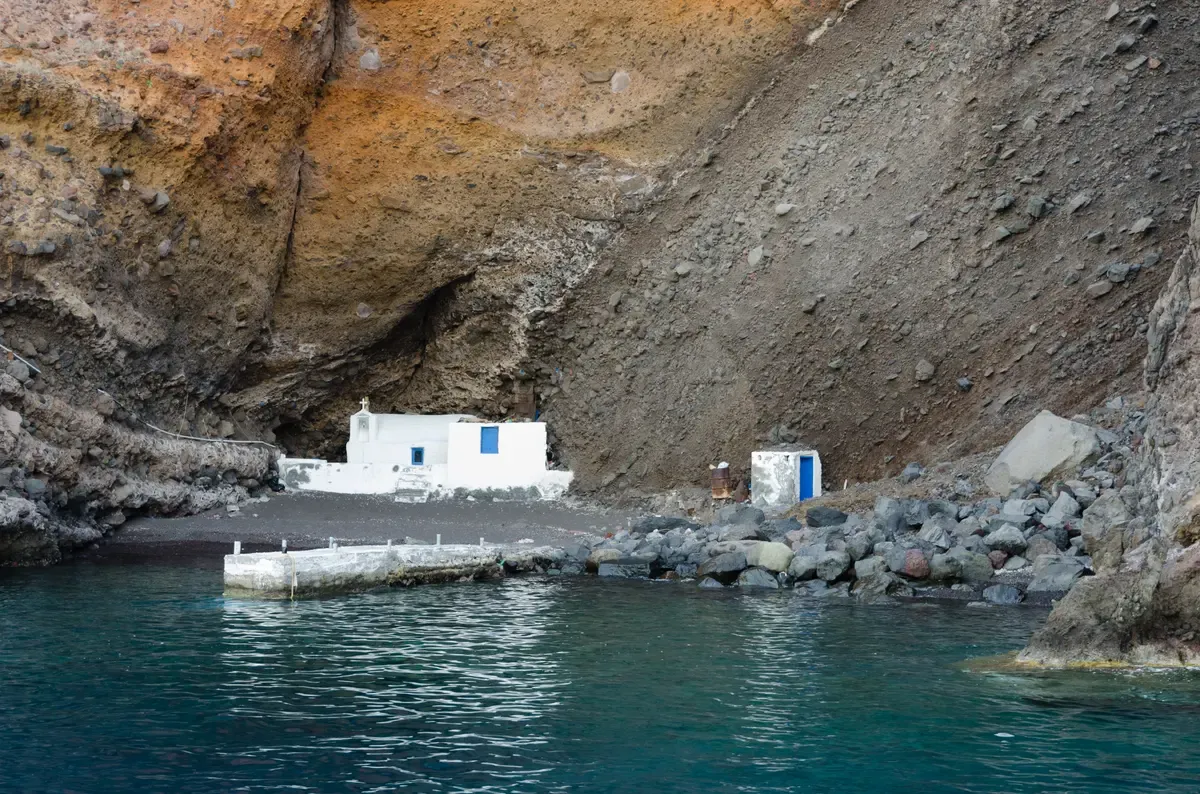 Small white chapel at sea level under a caldera cliff on Santorini, reached on a catamaran cruise